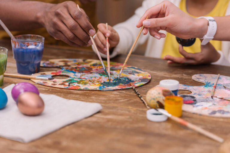 cropped image of african american parents and daughter putting paint brushes on palette, easter